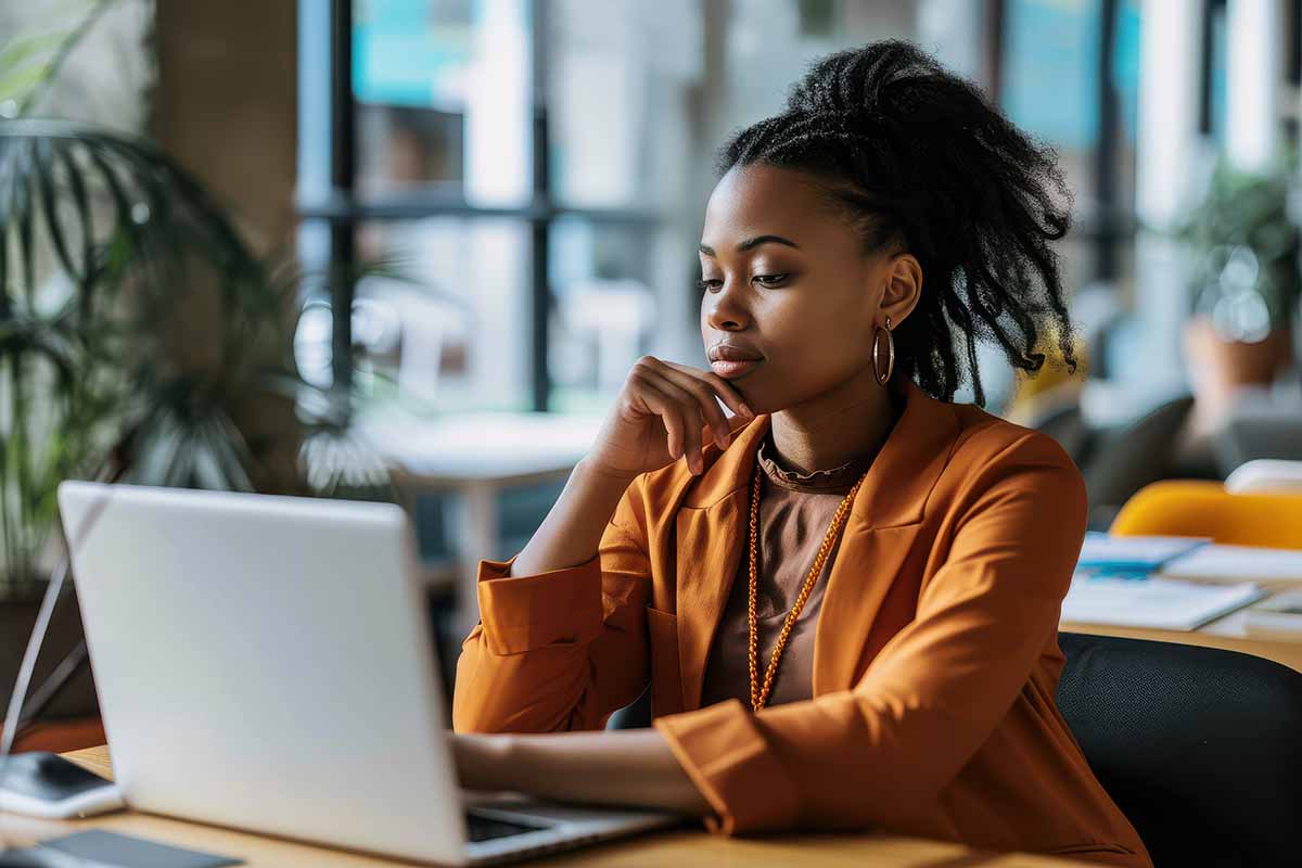 A young African American businesswoman sitting at a desk in an office setting looking at a laptop screen.