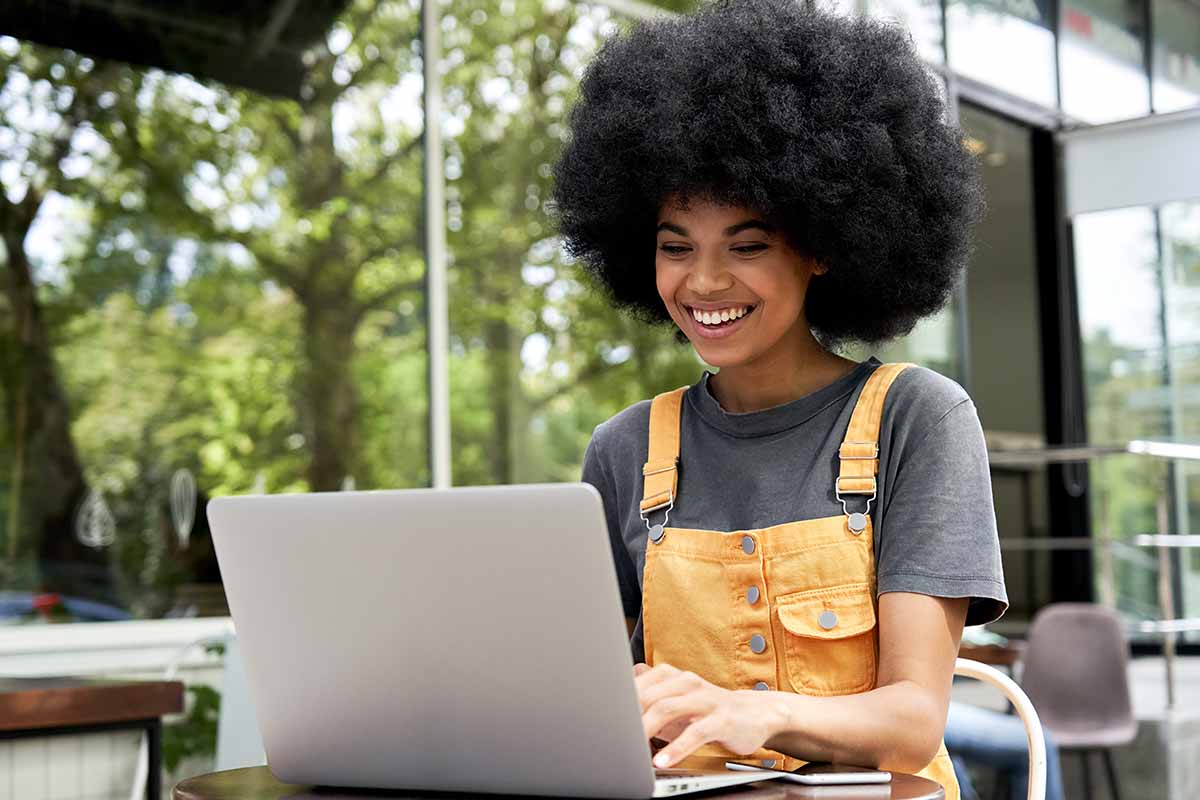 Smiling African American lady working on a laptop outside a café. 