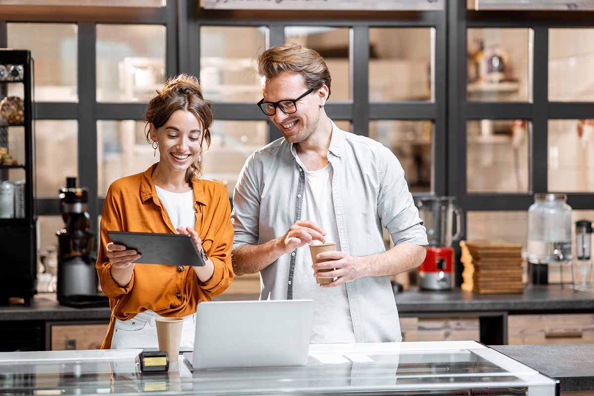 Two smiling young shop owners having a discussion while standing with a digital tablet at the counter of the shop. 