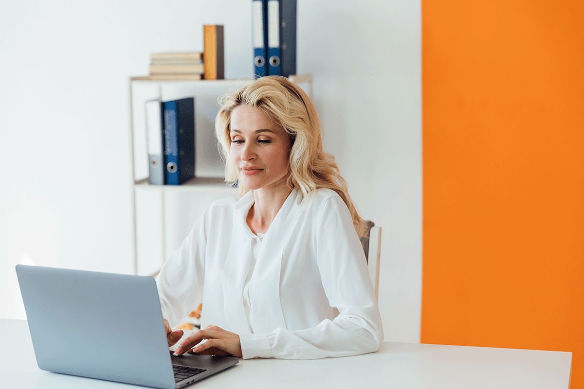 Businesswoman sitting at a white desk working on a laptop.