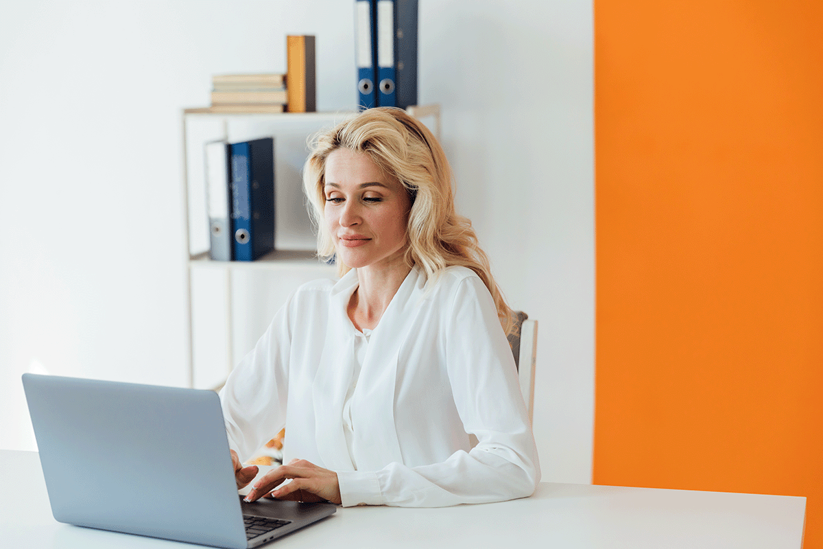 A businesswoman sitting at a white desk working on a laptop.