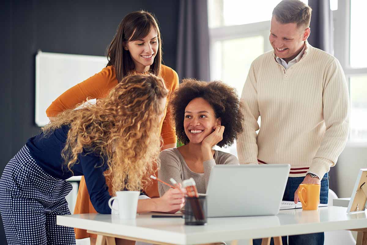 A smiling group of young colleagues working together around a desk and laptop.