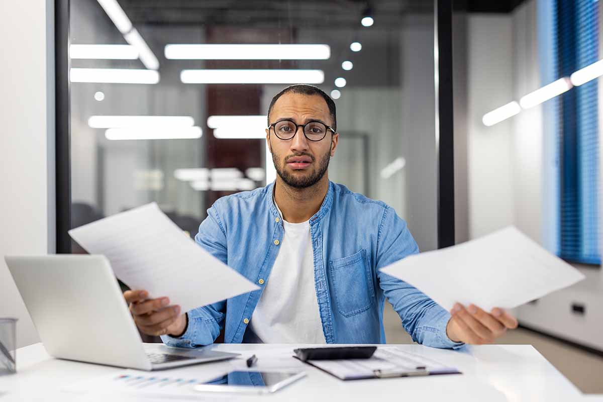 Confused businessman analyzing paperwork in modern office.