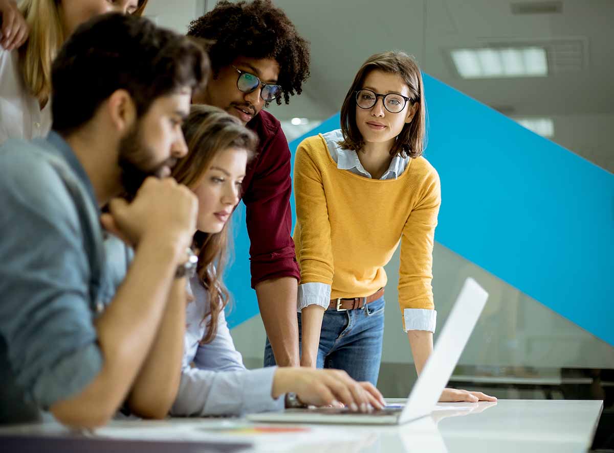 A group of young colleague looking at a laptop screen together.