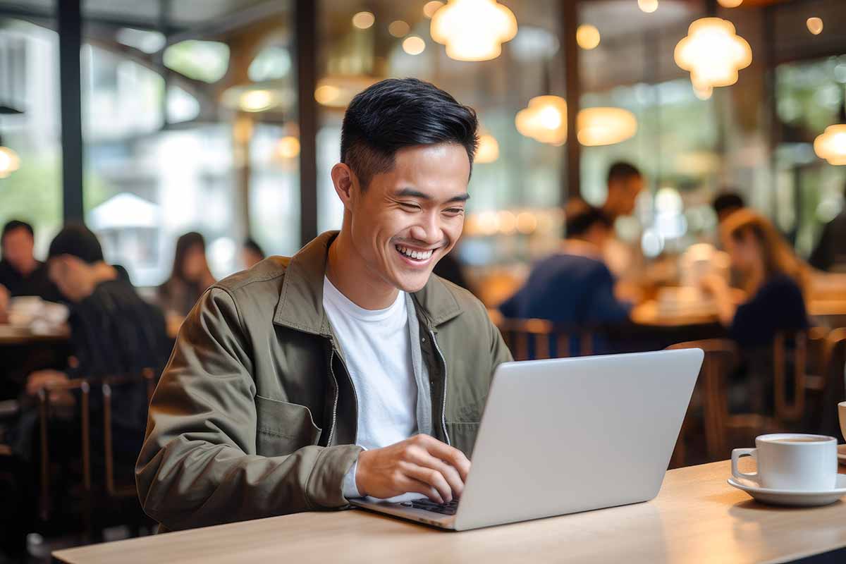 Asian man working on a laptop in a busy café in the city.